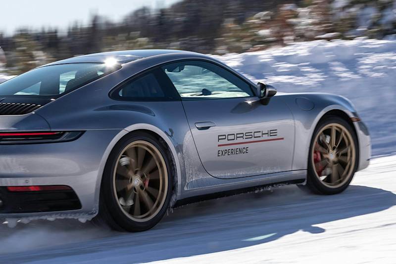 Silberner Porsche rast durch verschneite Landschaft mit eleganten Linien und Porsche Experience an der Seite, deutet hohe Geschwindigkeit an.