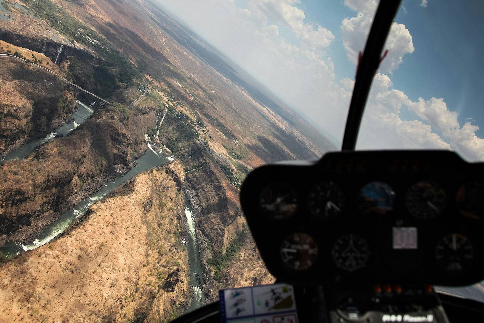Porsche über einem windenden Fluss und einer felsigen Schlucht unter bewölktem Himmel.