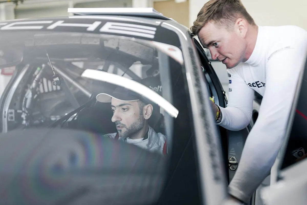 Zwei Männer in Rennkleidung, einer im Porsche-Auto, der andere lehnt sich zum Reden hinein.
