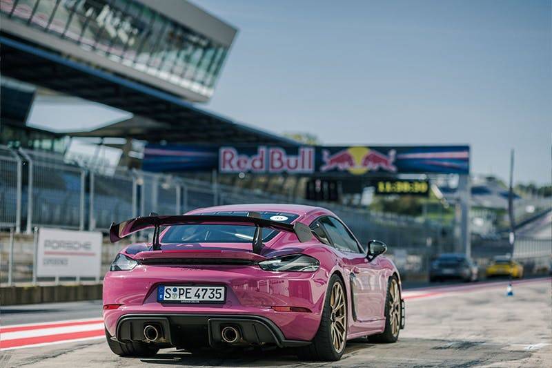 Porsche Sportwagen auf Rennstrecke in der Nähe des Red Bull Schildes, umgeben von Tribünen unter klarem Himmel.