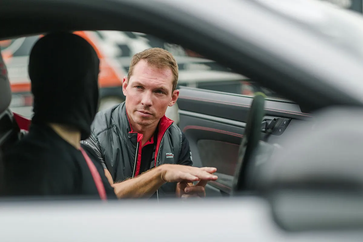 Person mit schwarzer Maske hört zu, als Mann im Porsche spricht.