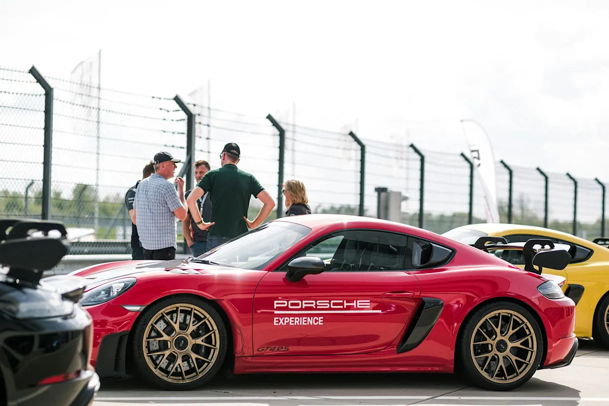 Red Porsche GT4 RS sports car on racetrack with people nearby.
