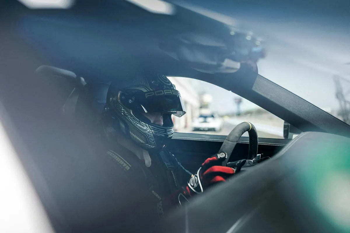 Rennfahrer mit Ausrüstung und Helm konzentriert sich hinter dem Porsche-Lenkrad auf der Rennstrecke.