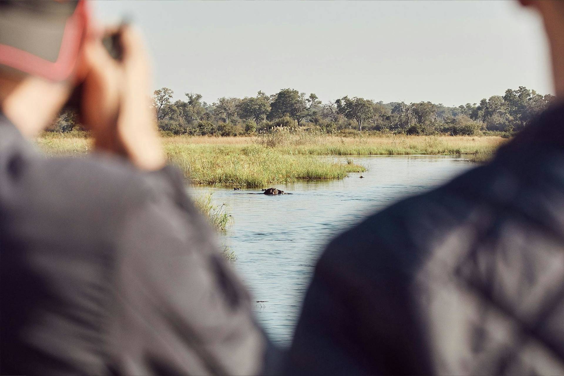 Zwei Leute beobachten einen Porsche im Fluss mit Bäumen und Himmel.