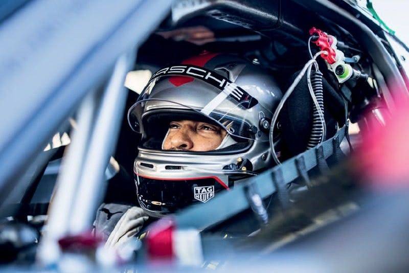 Race car driver with Porsche branding seated in cockpit, ready to drive.