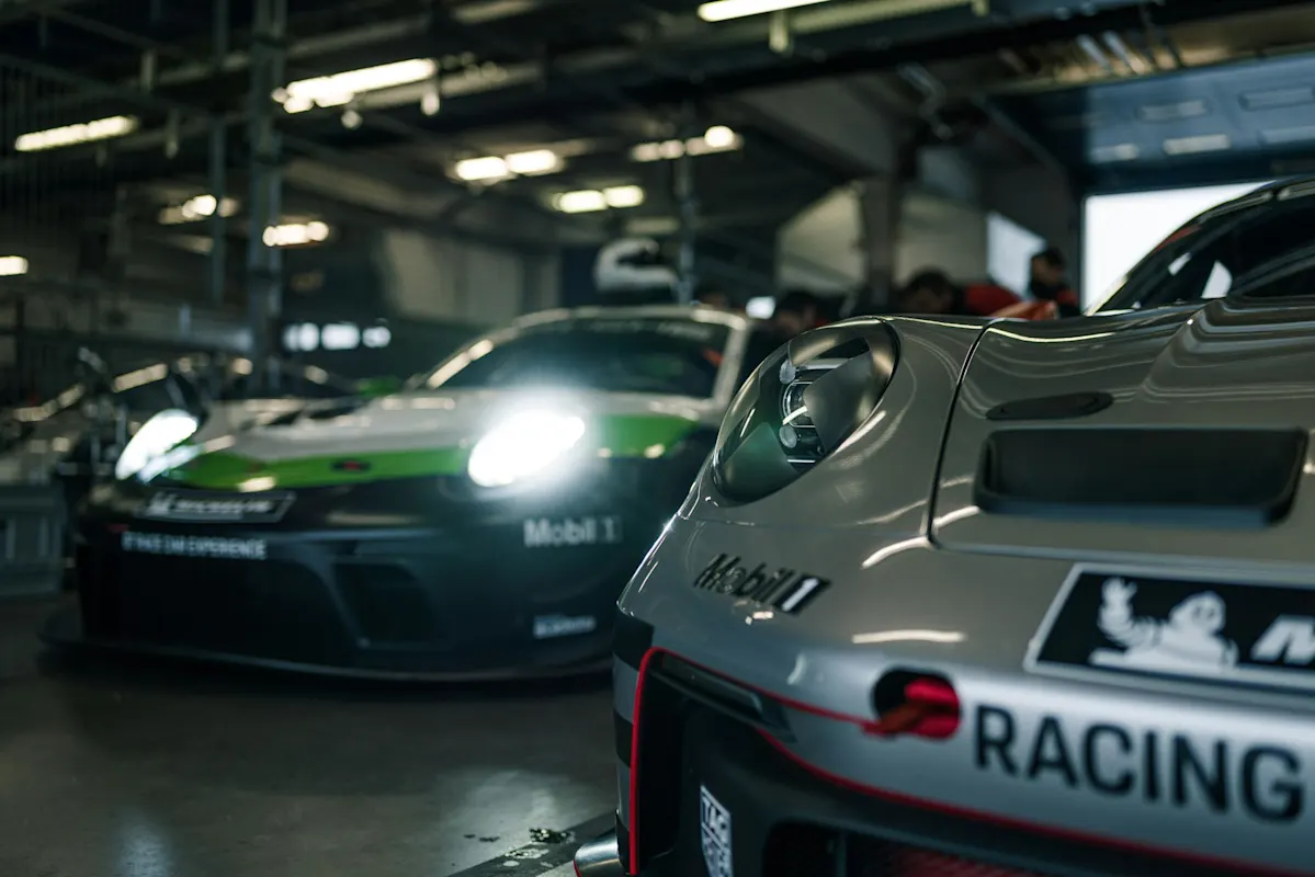 Close-up of a silver Porsche racing car in a dimly lit garage with another Porsche in the background.