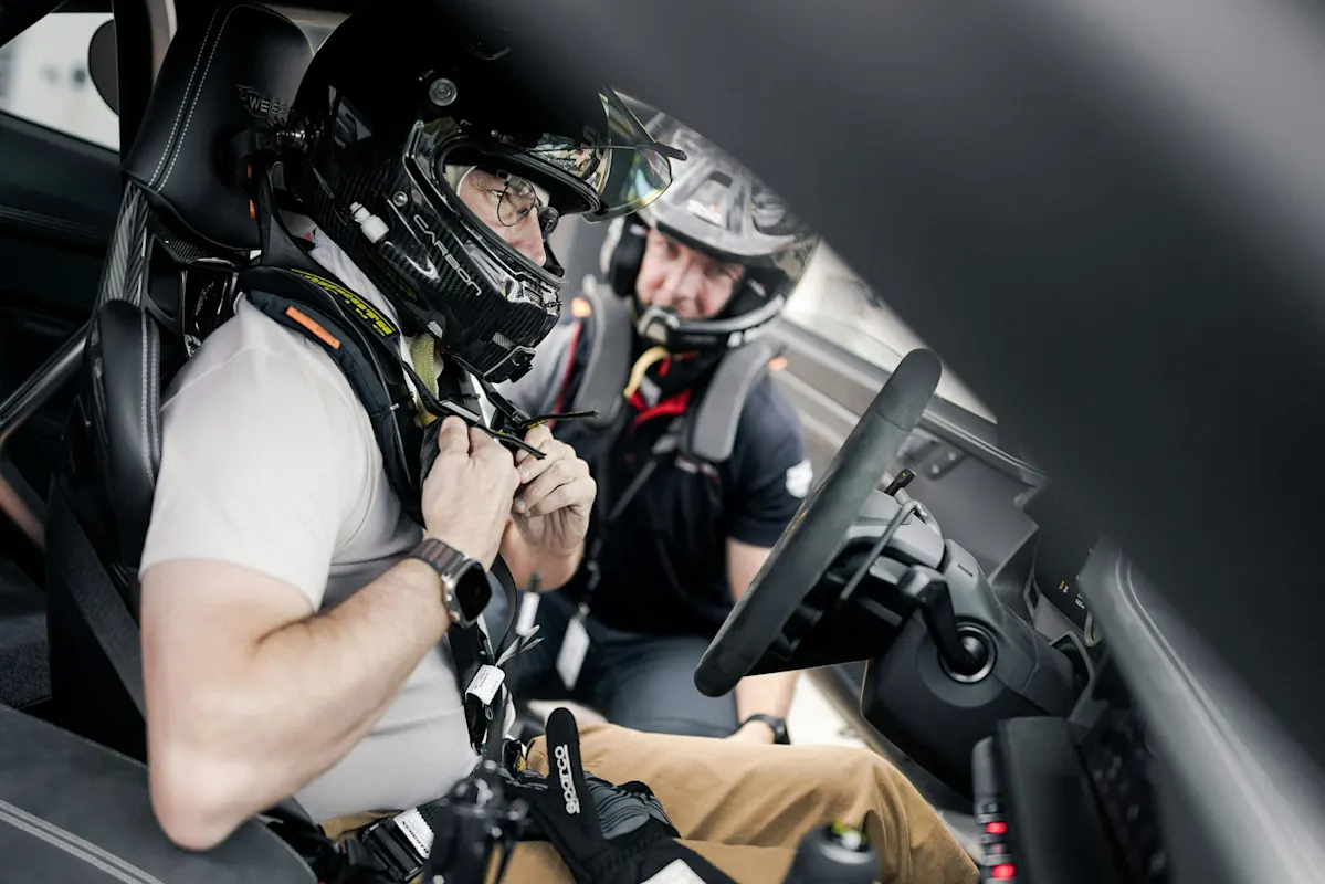 Person schnallt Sicherheitsgurt in einem Porsche an, Assistenz durch Helmpflichtige.