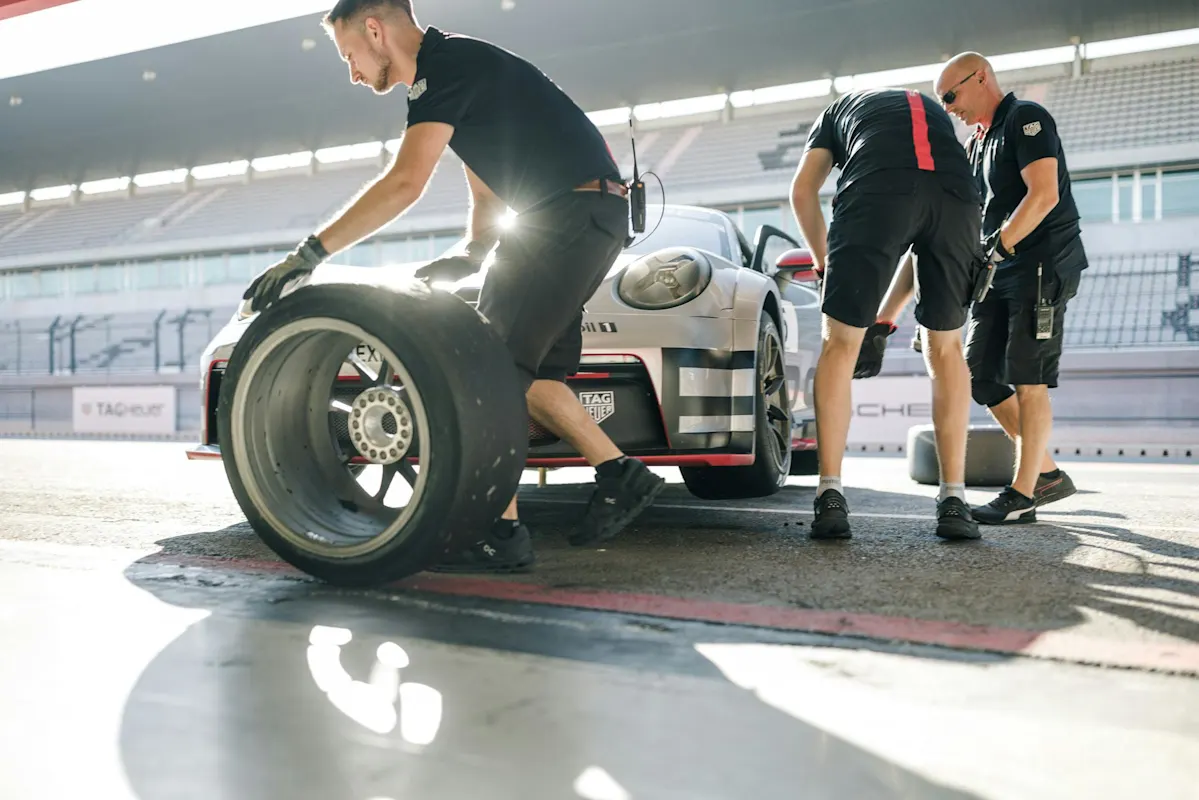 Porsche pit crew changing race car tires at sunny track.