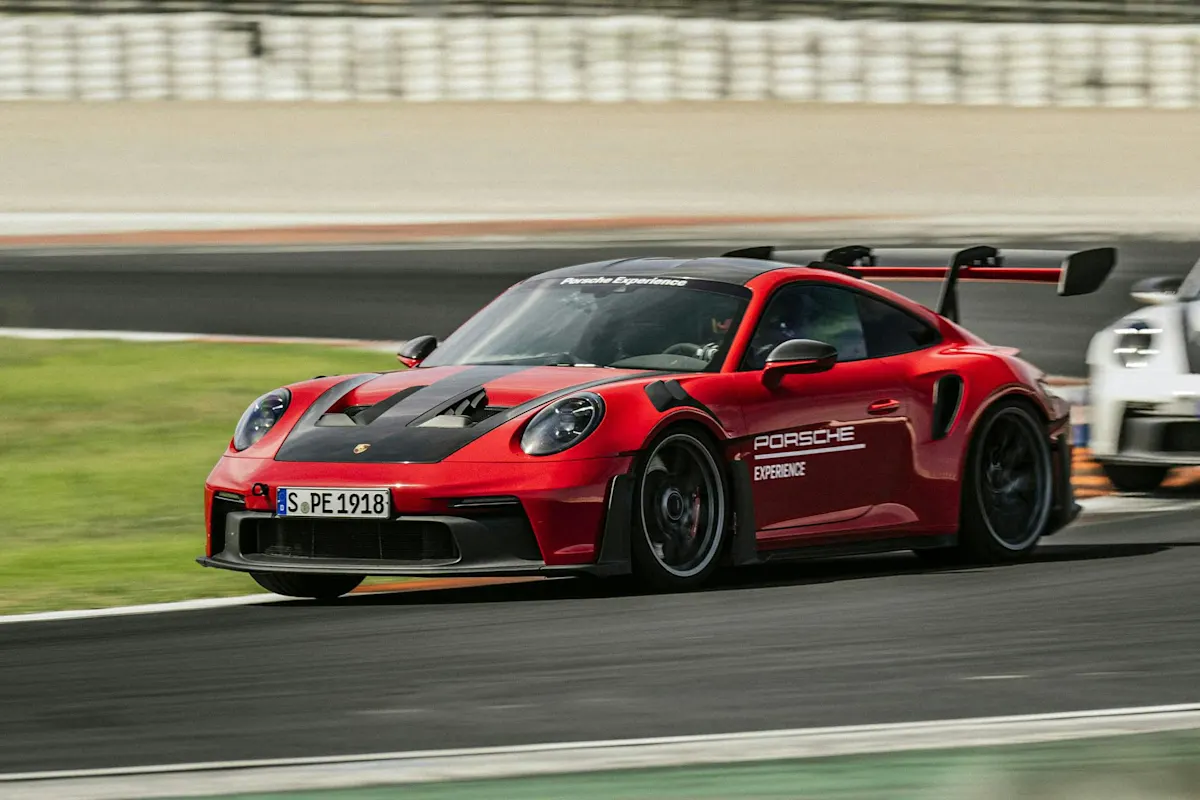 Roter Porsche Sportwagen mit schwarzen Akzenten und Porsche Experience Branding rast mit Bewegungsunschärfe auf der Rennstrecke.