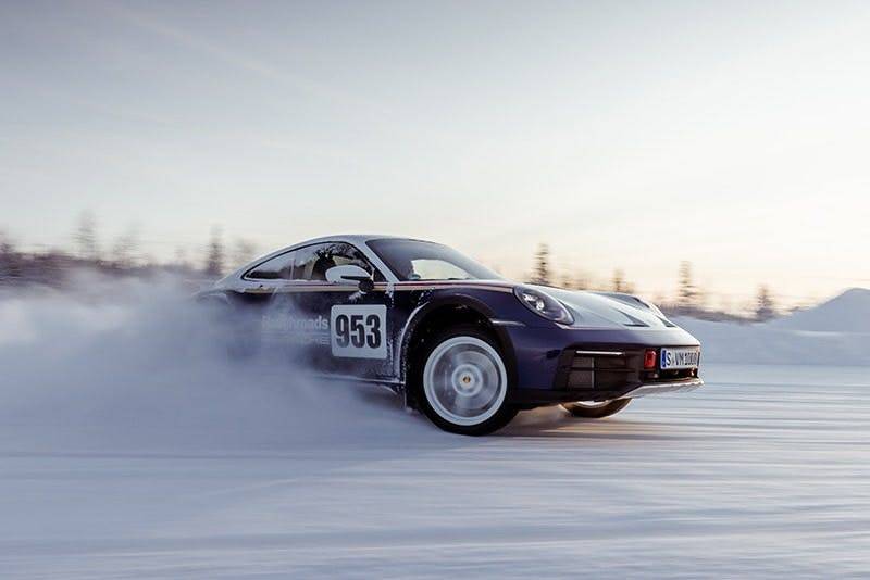 Porsche 953 driftet im Schnee zwischen Bäumen und erzeugt Schneewolke.