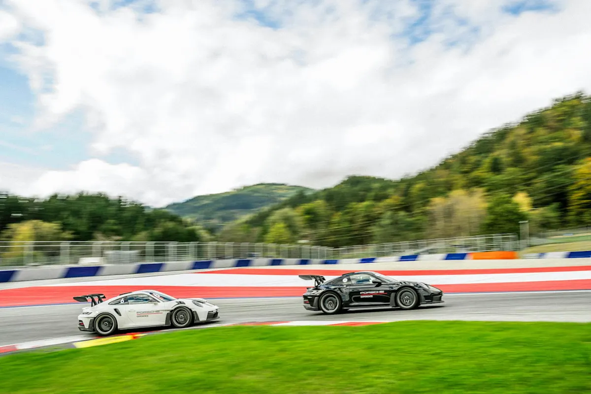 Porsche racing car speeding on track amid green hills under cloudy sky.