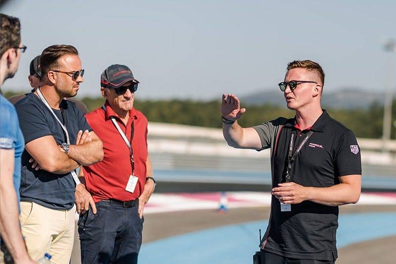 A man in black gestures talking to three men on a sunny outdoor track.