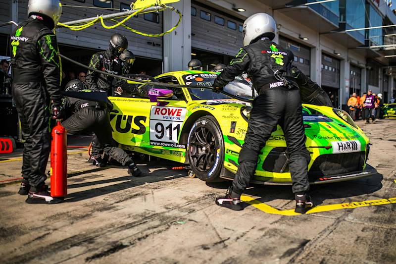 Porsche-Pitcrew bedient einen hellgelben und grünen 911-Rennwagen während eines Boxenstopps mit Equipment.