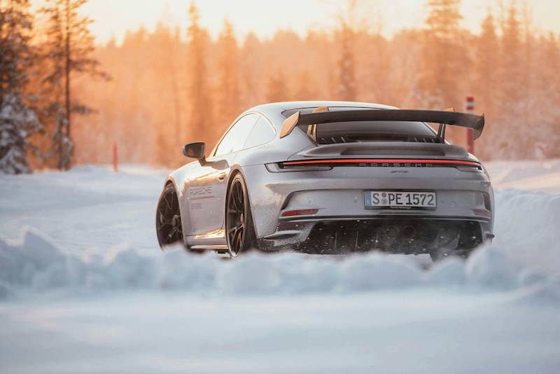 A silver Porsche sports car in snow, trees, and sunset.