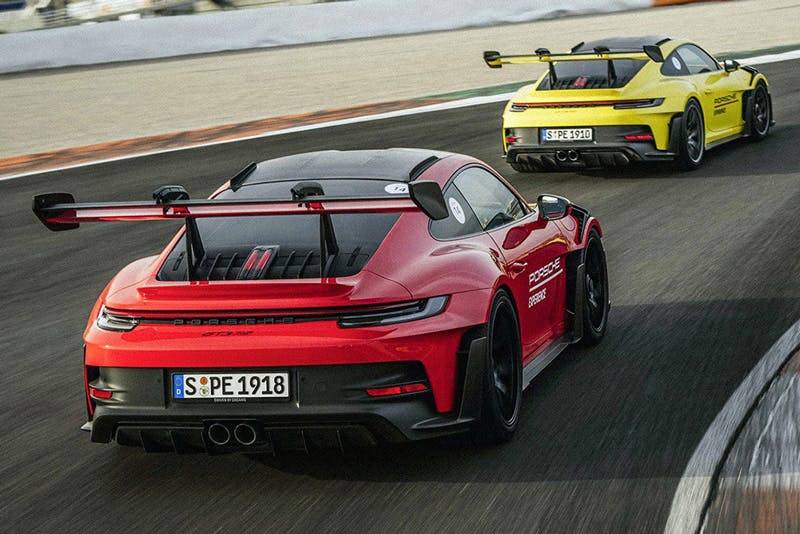 Porsche sports cars with rear wings in red and yellow racing on track at high speed.