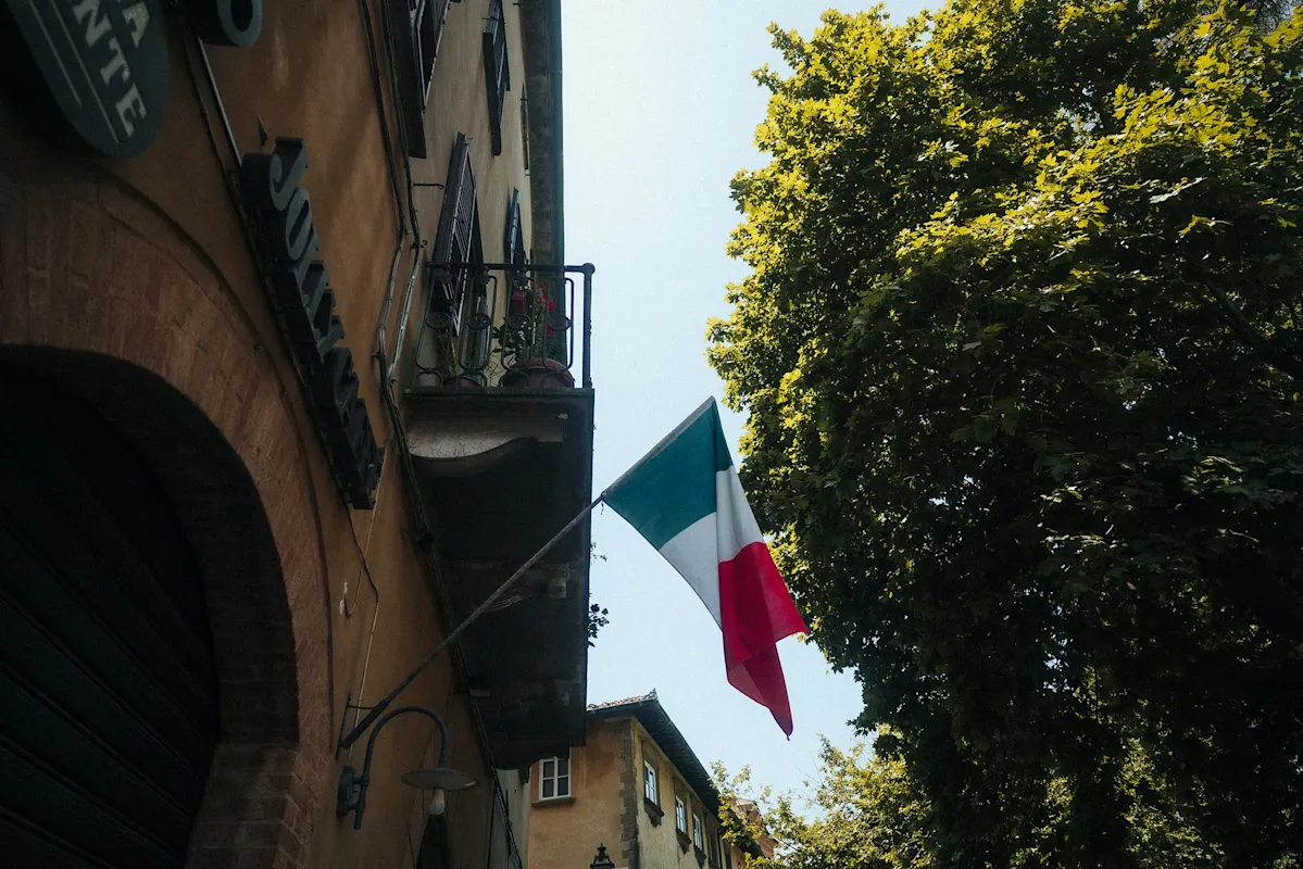 Italienische Flagge auf Balkon, Bäume vor hellem Himmel.