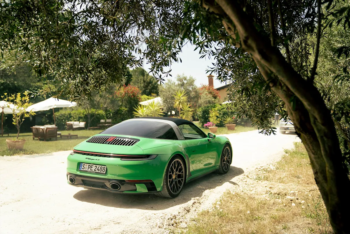 Green Porsche convertible on sunny dirt road with trees and umbrellas.