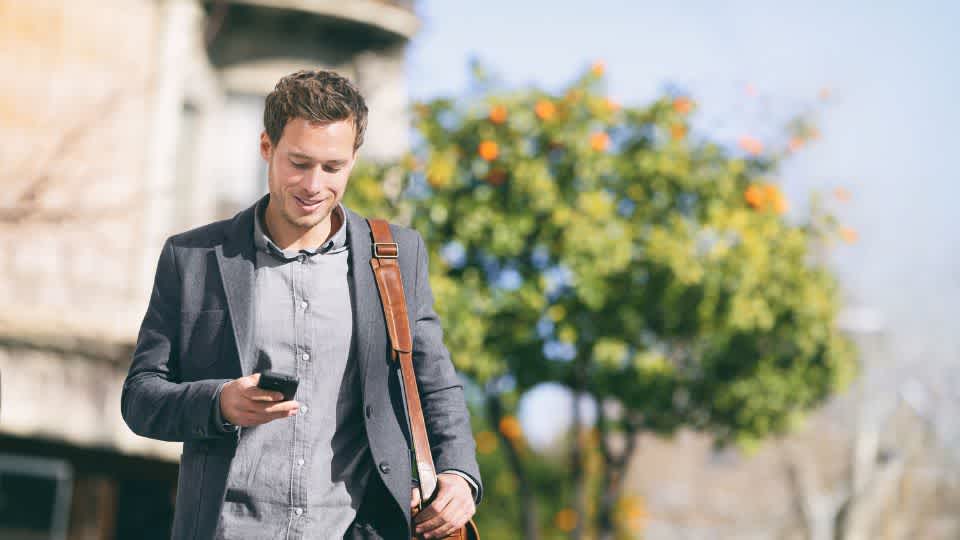 This picture shows a man walking outside and looking at his mobile phone. . It serves as an illustration of the Semplates Case Study with Emma App.