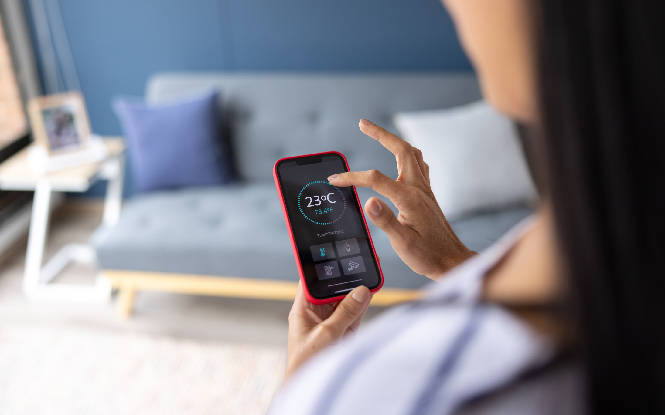 A woman adjusting the temperature on her smart thermostat via her cell phone