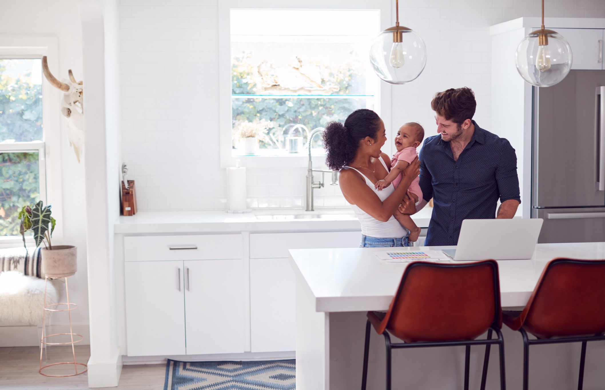 A stock image of a couple with a baby smiling in their kitchen in their home