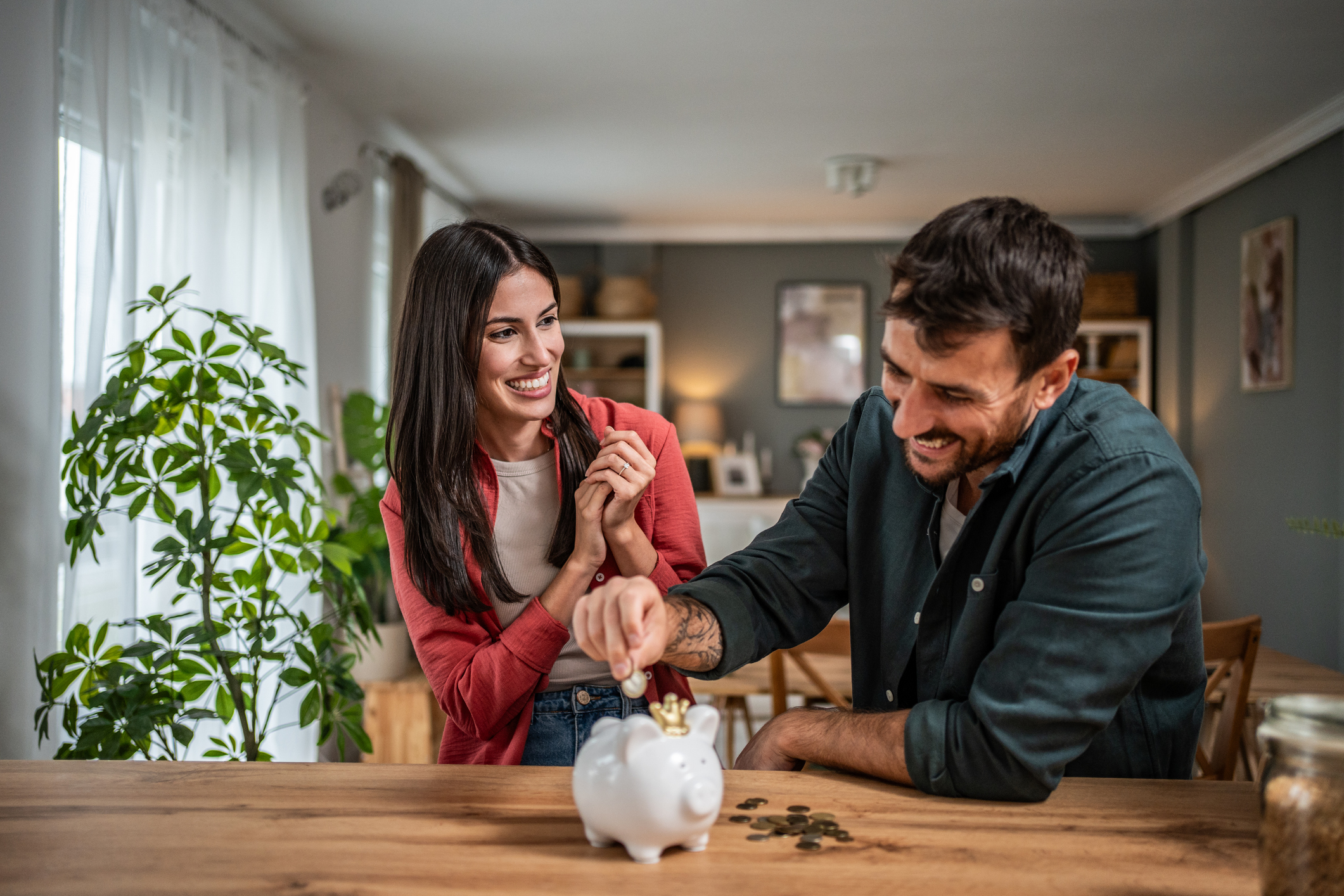 A couple in their home, smiling and putting coins in a piggy bank