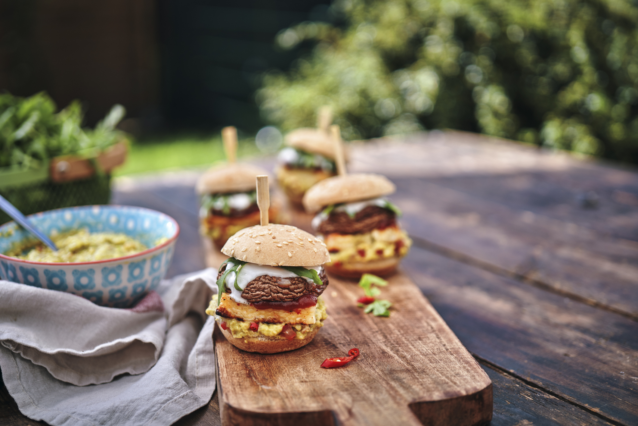 A plant-based veggie burger sitting on a picnic table at a summer barbecue.