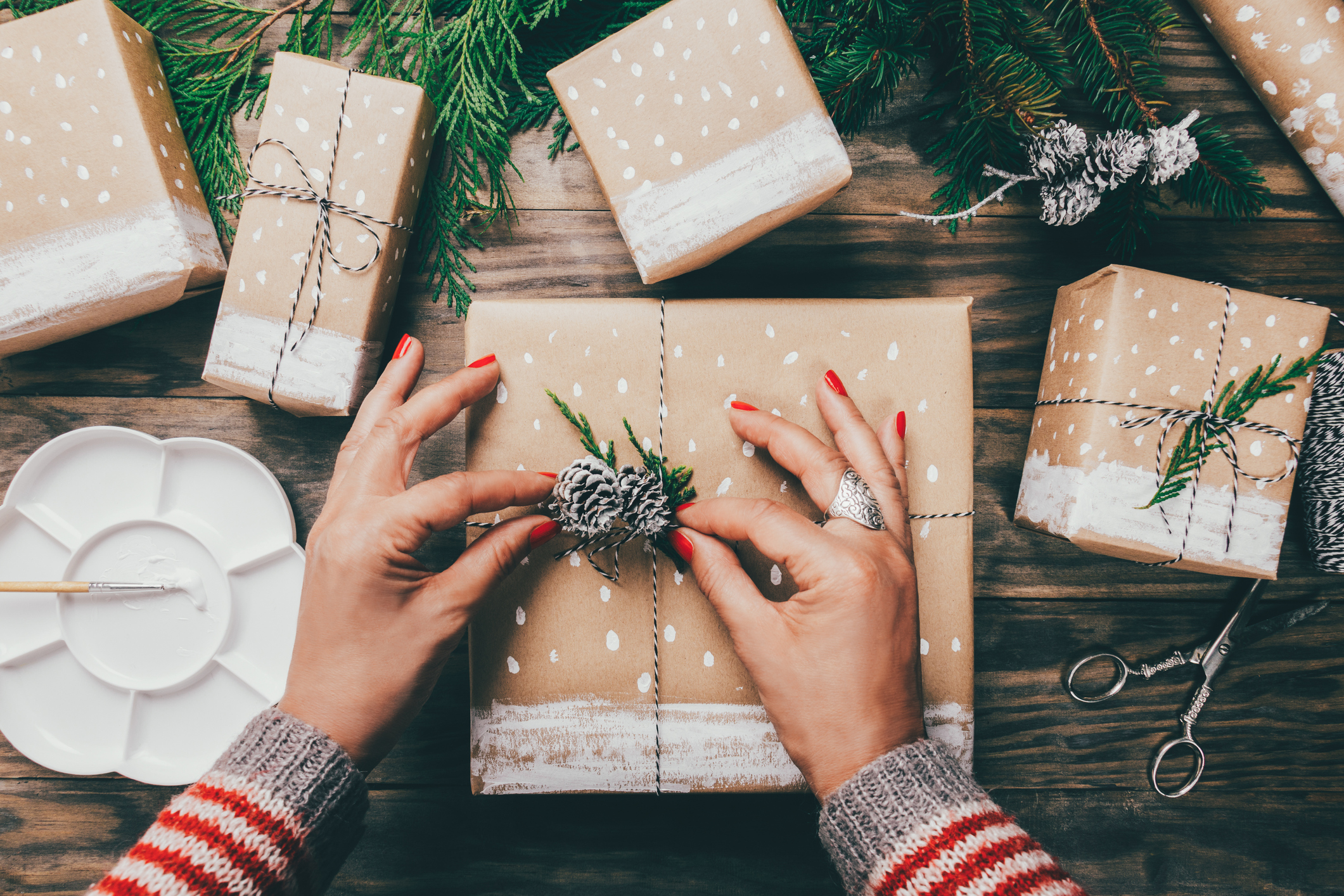 A woman wrapping holiday gifts with paper and pinecones.