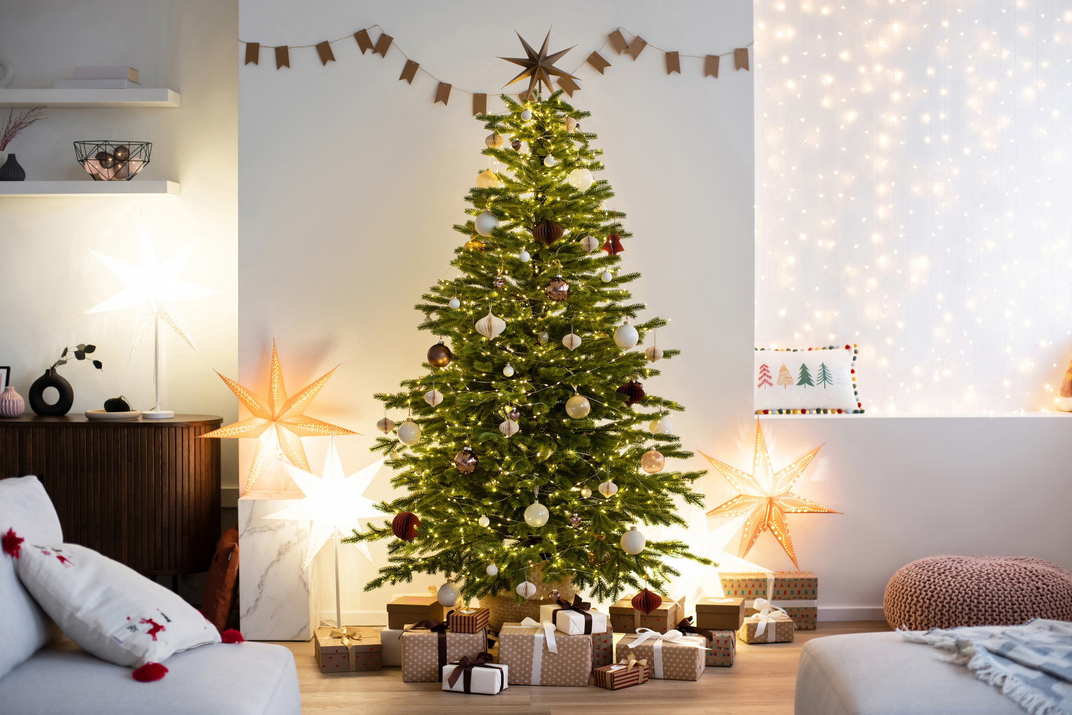 A Christmas tree lit up inside a home, surrounded by presents and lit-up stars.