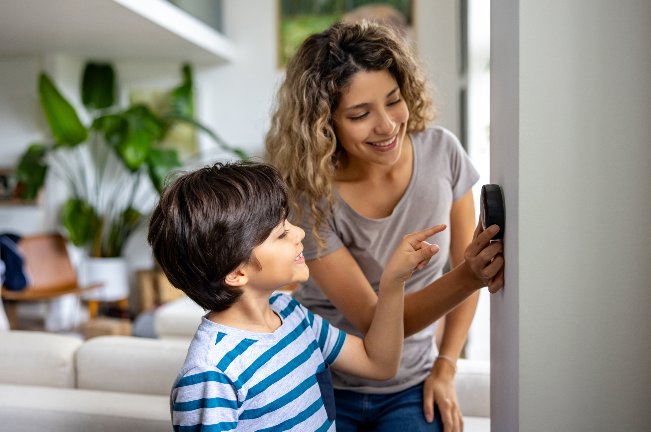 A mother and son adjusting the smart thermostat in their home