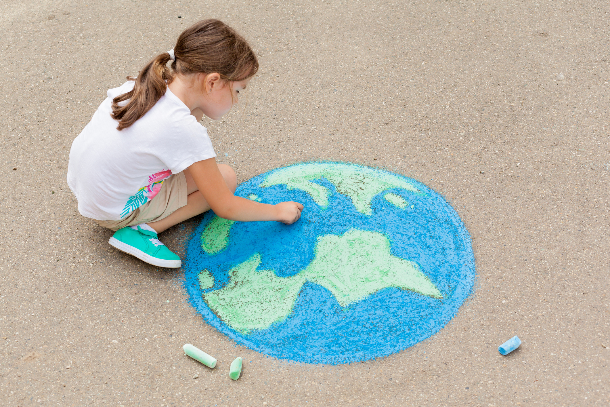 A young girl drawing the Earth in chalk on the sidewalk.
