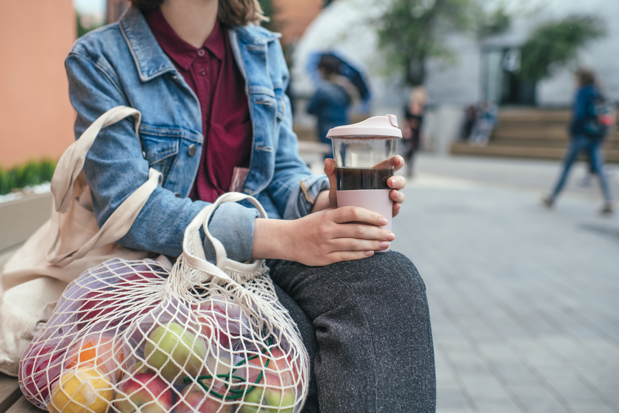 Woman holding a reusable coffee cup and mesh produce bag.