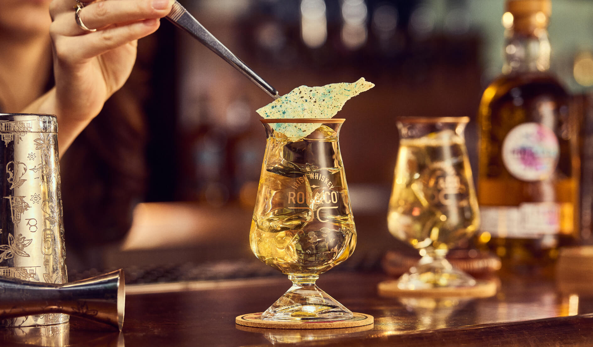 Bartender uses tweezers to place a blue garnish on a Roe & Co Irish whiskey cocktail at the Power House Bar.