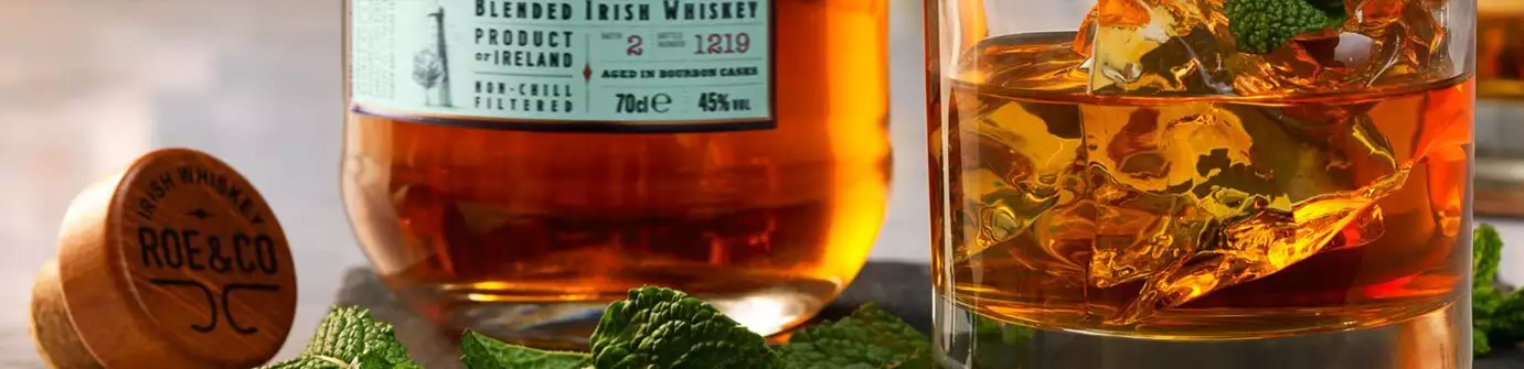 A bottle of Roe & Co Irish Whiskey beside a glass with ice and mint, with the branded cork in the foreground.