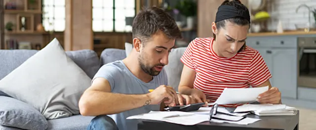 A man and woman reviewing bills and financial documents while calculating expenses at home.