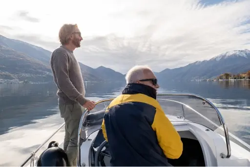 Two men riding a smaller boat on a lake with mountains in the background