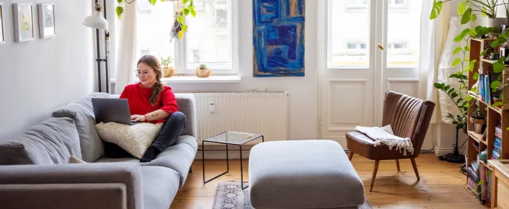 Woman working on laptop in a cozy, sunlit living room.