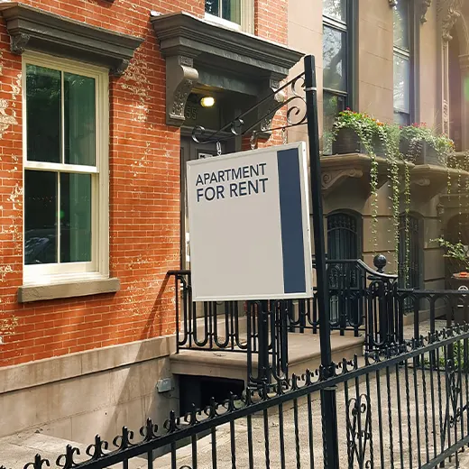 A "For Rent" sign hangs outside a brick building with decorative iron fen fencing