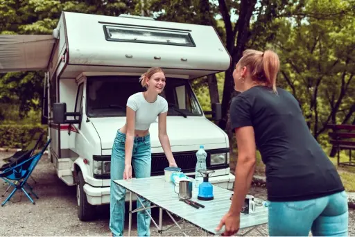 Two women smiling and enjoying themselves while setting up camp around their RV