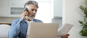 Man reviewing financial documents while talking on the phone about debt collection.