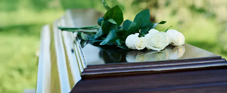 A casket with white roses on top in an outdoor setting.