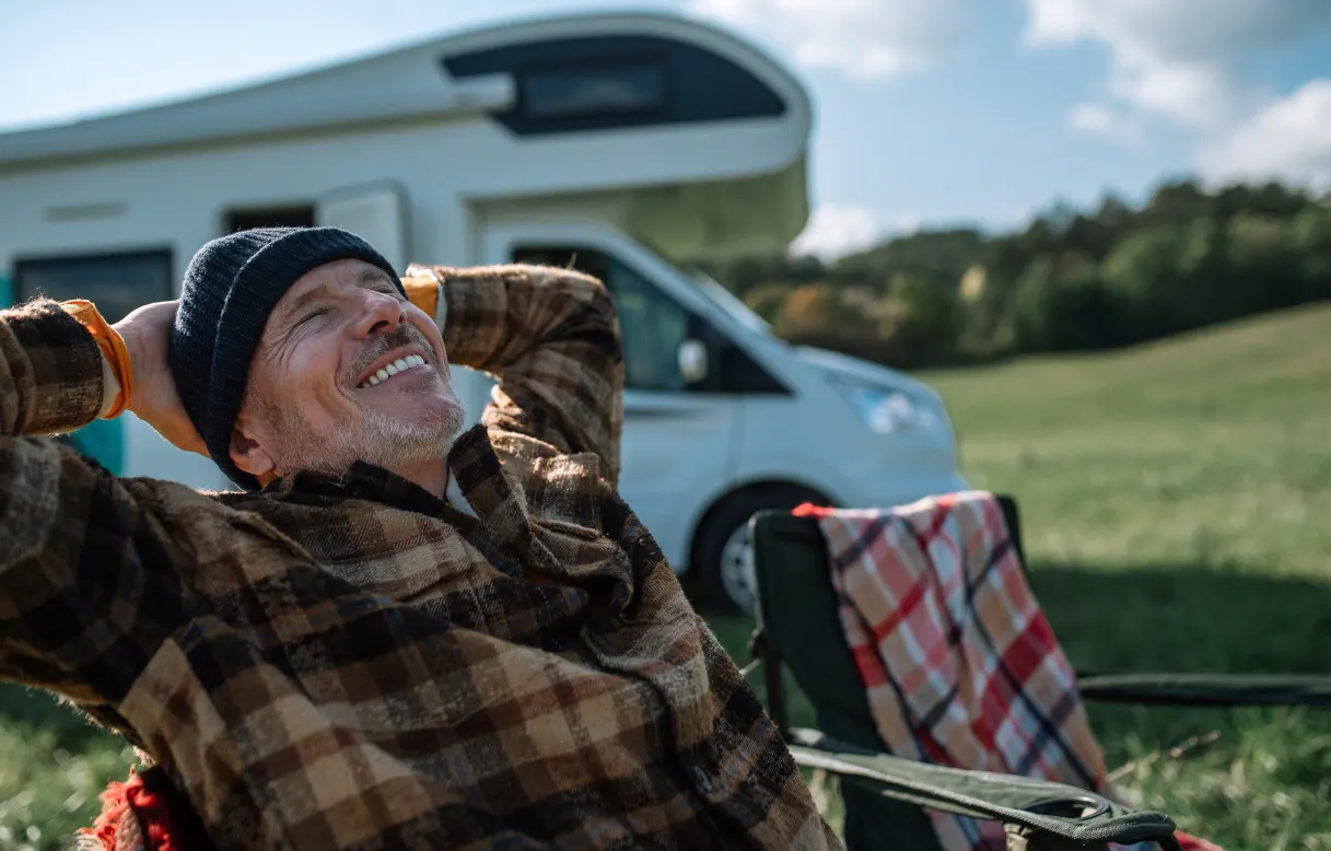 A man relaxing in a chair outside his camper van in a grassy field.