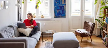 Woman working on laptop in a cozy, sunlit living room.