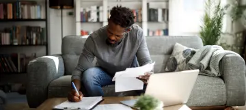 Man sitting on couch weighing out the pros and cons of debt consolidation - OneMain Financial