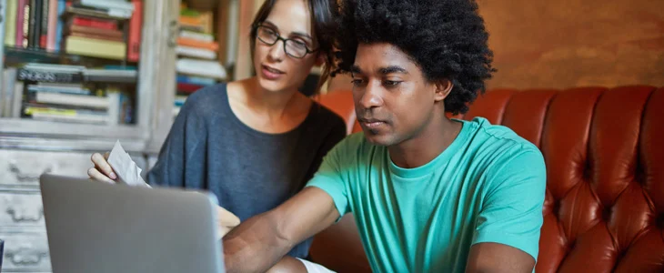 A young man and a woman are working together on a laptop in a cozy setting.