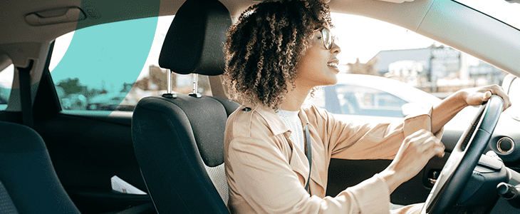 Inside of a car being driven by a smiling lady with cars in the background
