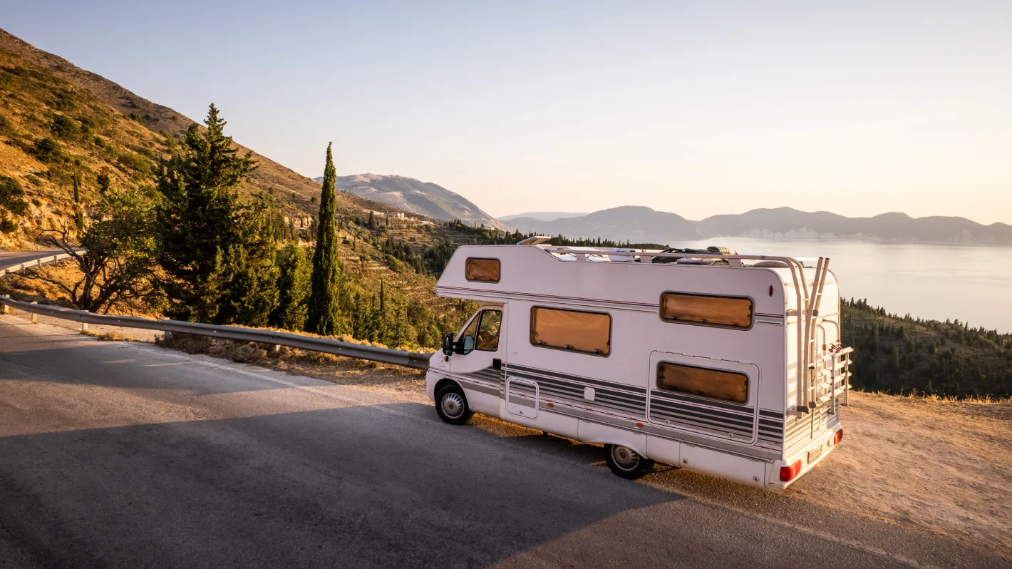 A camper van on a mountain road at sunset.