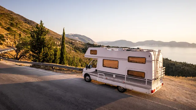 A camper van on a mountain road at sunset.