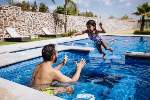 A man in the pool with his arms out ready to catch his daughter jumping into the pool