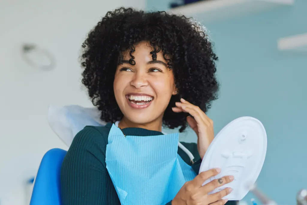 A woman with a bright smile holding a mirror, sitting in a dental clinic.