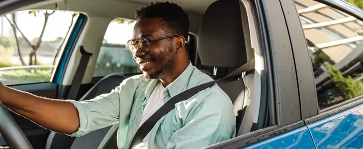 A man wearing a seat belt while driving a car on a sunny day.